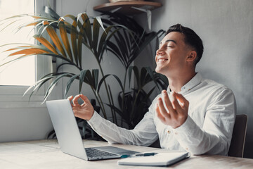 Serene office male employee sit at desk relaxing doing yoga, practice meditation to reduce stress relief fatigue feel internal balance at workplace, improve mindfulness, maintain mental health concept