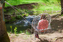 Child Sitting On Hammock Near Creek At Forest On Summer Day.
