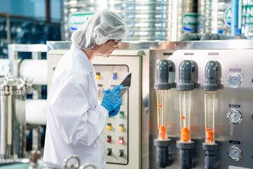 Female worker inspecting water bottle on production line in spring water factory