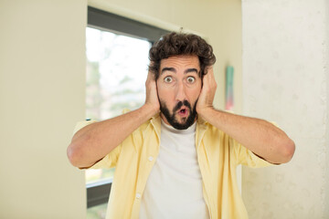 Wall Mural - young crazy bearded man looking excited and surprised, open-mouthed with both hands on head, feeling like a lucky winner