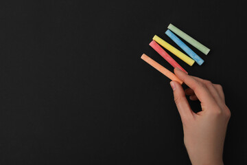 Multicolored pieces of chalk in hand on black background, place for text