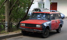 Old Soviet Rusty Black And Red Car Stands In The Courtyard Of A Residential Building, Dybenko Street, St. Petersburg, Russia, July 10, 2023