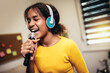 © Mediteraneo - Cute preteen black girl holding a microphone singing karaoke at home, recording songs for a contest. Children's lifestyle concept