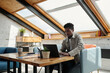 © pressmaster - Young serious African American businessman looking at laptop screen while sitting by workplace in loft studio and working over new project