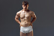 Handsome young man with muscular body, relief torso. Model posing shirtless in underwear against grey studio background. Concept of man's beauty, sportive and healthy lifestyle, athletic body
