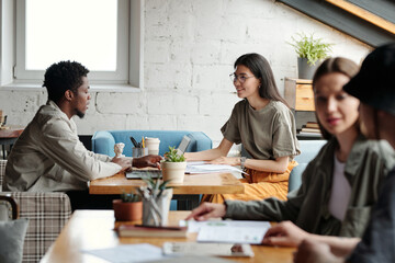 Aufkleber - Focus on two young intercultural brokers looking at each other during discussion of financial data while sitting by table in coworking space