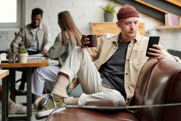 Aufkleber - Young serious male white collar worker in casualwear texting in smartphone or looking through messages while sitting on couch
