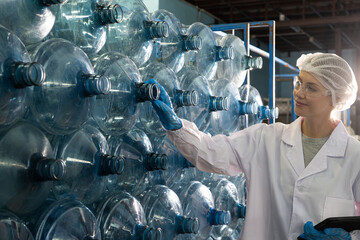 Caucasian women scientist with lab cote inspect quality of drinking water inside of the production line factory while using digital tablet to check cleanliness and standard, quality assurance