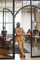 Aufkleber - Young confident African American businessman in beige formalwear looking at camera while standing in arch shaped door of coworking area