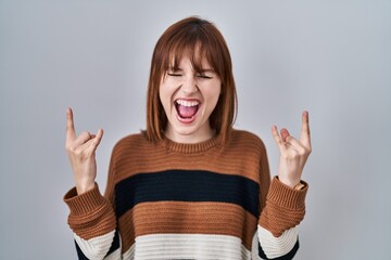 Wall Mural - Young beautiful woman wearing striped sweater over isolated background shouting with crazy expression doing rock symbol with hands up. music star. heavy music concept.