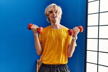 Sticker - Young blond man smiling confident using dumbbells training at sport center