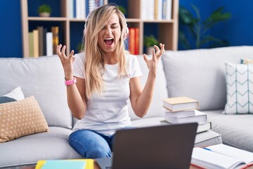 Canvas Print - Young blonde woman studying using computer laptop at home crazy and mad shouting and yelling with aggressive expression and arms raised. frustration concept.