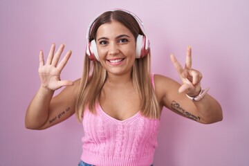 Wall Mural - Young blonde woman listening to music using headphones showing and pointing up with fingers number eight while smiling confident and happy.