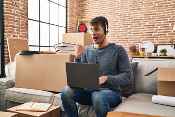 Poster - Young hispanic man working with laptop at new home pointing thumb up to the side smiling happy with open mouth