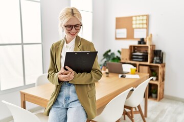 Wall Mural - Young blonde woman business worker smiling confident holding clipboard at office