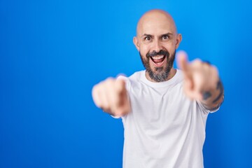 Hispanic man with tattoos standing over blue background pointing to you and the camera with fingers, smiling positive and cheerful