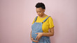 Young pregnant woman touching belly over isolated pink background