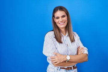 Poster - Hispanic young woman standing over blue background happy face smiling with crossed arms looking at the camera. positive person.