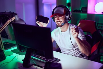 Poster - Hispanic man with beard playing video games with smartphone smiling happy pointing with hand and finger to the side