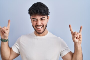 Poster - Hispanic man with beard standing over white background shouting with crazy expression doing rock symbol with hands up. music star. heavy music concept.