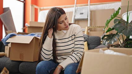 Wall Mural - Young beautiful hispanic woman sitting on sofa with serious expression at new home