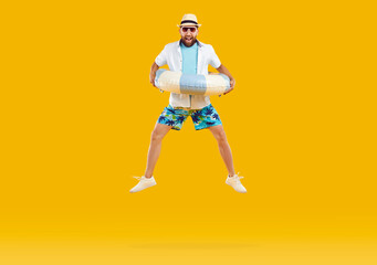 Happy funny man in summer clothes and sunglasses holding inflatable beach ring and jumping on trampoline high in air isolated on orange yellow color studio background. Summer holiday, vacation concept
