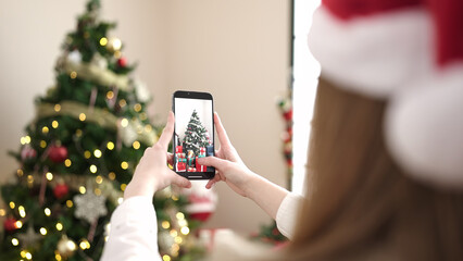 Poster - Young blonde woman make photo to christmas tree by smartphone at home