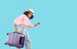 Child going on summer holiday. Happy kid with travel bag hurries to board the plane. Pretty Black girl in panama hat, jeans and pink blouse with suitcase walking isolated on blue copy space background