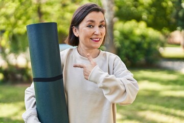 Poster - Middle age hispanic woman holding yoga mat at the park smiling happy pointing with hand and finger