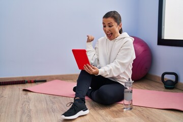 Wall Mural - Middle age hispanic woman training using tablet pointing thumb up to the side smiling happy with open mouth