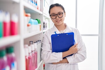 Canvas Print - Young chinese woman pharmacist smiling confident holding clipboard at pharmacy