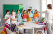 © Studio Romantic - Children holding colored paper sheets together at school during session with school psychologist. Positive female psychologist conducts group therapy with elementary school students in form of game.