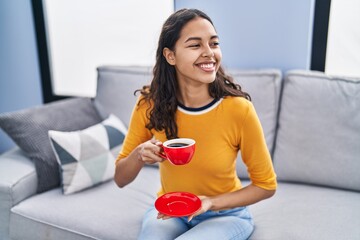 Sticker - Young african american woman drinking coffee sitting on sofa at home