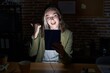 © Krakenimages.com - Blonde caucasian woman working at the office at night pointing to the back behind with hand and thumbs up, smiling confident
