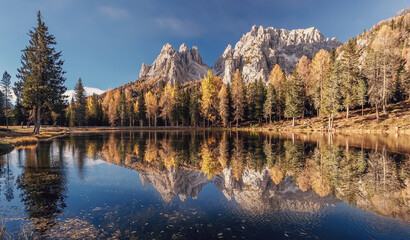 Fototapete - Incredible autumn scenery with reflections. Amazing autumn landscape in the mountains with yellow larches and lake glowing by sun and high mountain peaks behind. Antorno lake. Picture of Wild area.