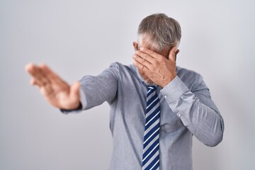 Poster - Hispanic business man with grey hair wearing glasses covering eyes with hands and doing stop gesture with sad and fear expression. embarrassed and negative concept.