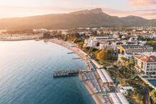 Indulge In A Captivating Visual Journey With Mesmerizing Aerial Shot, Revealing A Panoramic Vista Of Kemer's Hotels Harmoniously Nestled Between A Picturesque Sea Beach And Awe-inspiring Mountains.