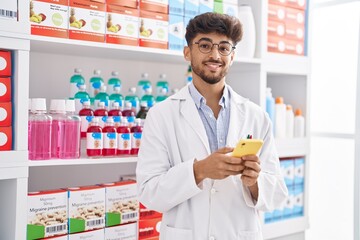 Poster - Young arab man pharmacist using smartphone standing at pharmacy