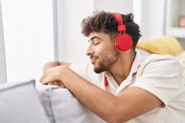 Wall Mural - Young arab man listening to music sitting on sofa at home