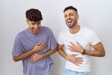 Wall Mural - Homosexual gay couple standing over white background smiling and laughing hard out loud because funny crazy joke with hands on body.