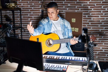 Canvas Print - Hispanic young man playing classic guitar at music studio showing middle finger, impolite and rude fuck off expression