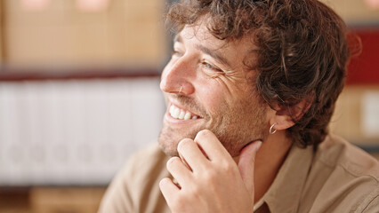 Young hispanic man ecommerce business worker sitting on table smiling at office