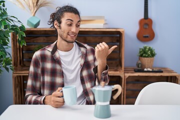 Poster - Young hispanic man drinking coffee from french coffee maker pointing thumb up to the side smiling happy with open mouth