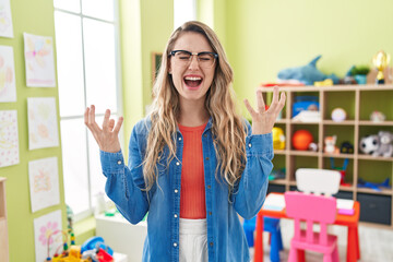 Wall Mural - Young caucasian woman working as teacher at kindergarten crazy and mad shouting and yelling with aggressive expression and arms raised. frustration concept.