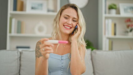 Sticker - Young blonde woman talking on smartphone holding pregnancy test smiling at home