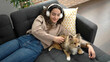 © Krakenimages.com - Young hispanic woman with dog listening to music lying on sofa at home