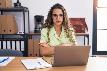 Wall Mural - Young hispanic woman working at the office wearing glasses skeptic and nervous, disapproving expression on face with crossed arms. negative person.