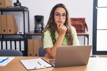 Sticker - Young hispanic woman working at the office wearing glasses looking confident at the camera with smile with crossed arms and hand raised on chin. thinking positive.