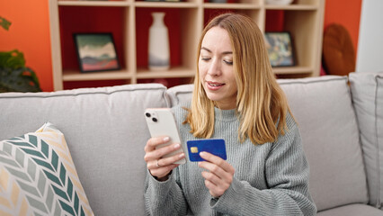 Poster - Young blonde woman shopping with smartphone and credit card sitting on sofa at home