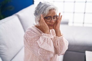 Poster - Middle age grey-haired woman suffering for headache sitting on sofa at home